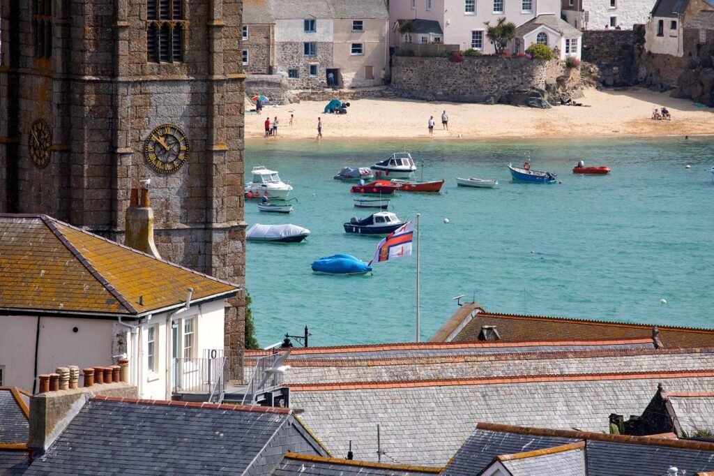 Coastal scene with boats, church tower, and people on a sandy beach.