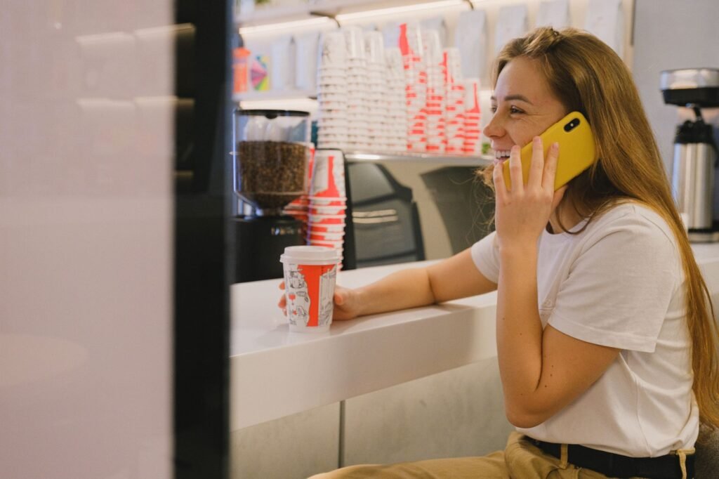 Smiling woman in coffee shop talking on smartphone, enjoying a hot drink.