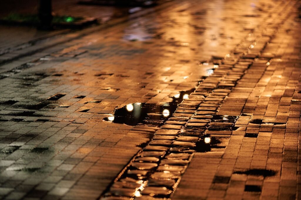 Moody night scene of rain-soaked cobblestones with reflections from streetlights.