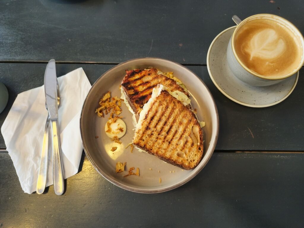Grilled sandwich and cappuccino on a wooden table, perfect for a casual cafe setting.