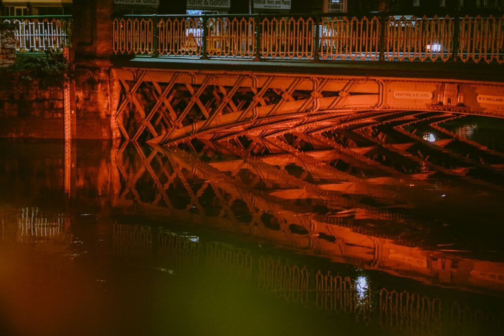 Steel bridge reflecting in water at night, creating a mesmerizing scene.