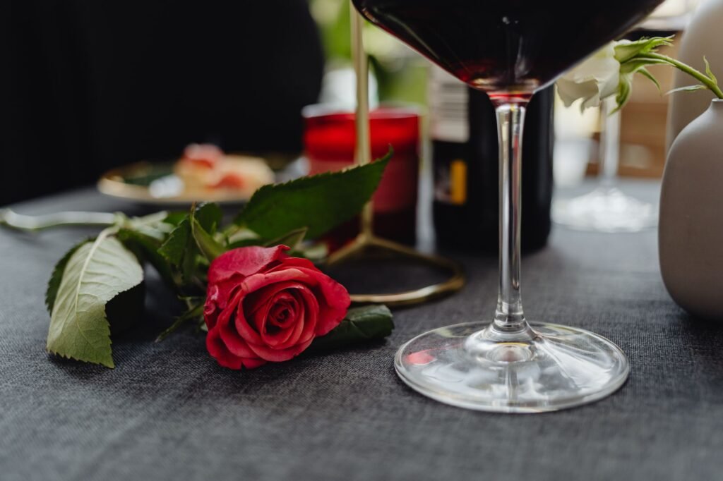 Close-up of a romantic table setting featuring a red rose and wine glass.