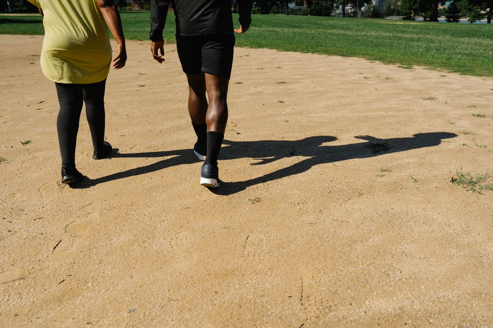 A man and woman walking on a sunny path in a park, casting shadows.