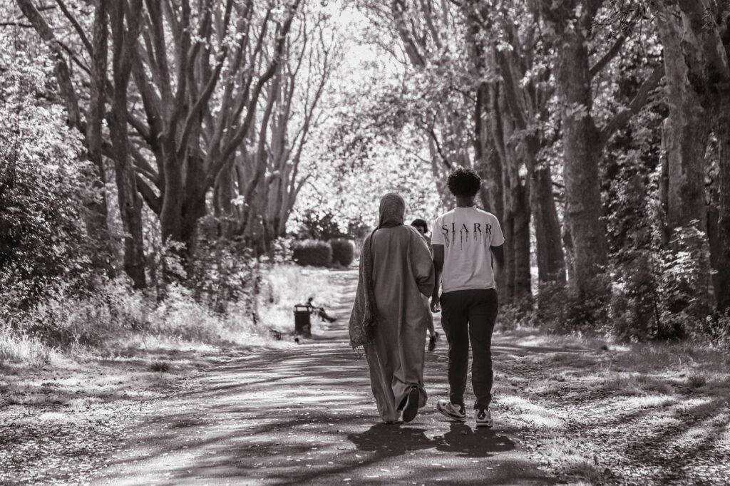 A couple walks through a serene tree-lined path in a park, captured in black and white.