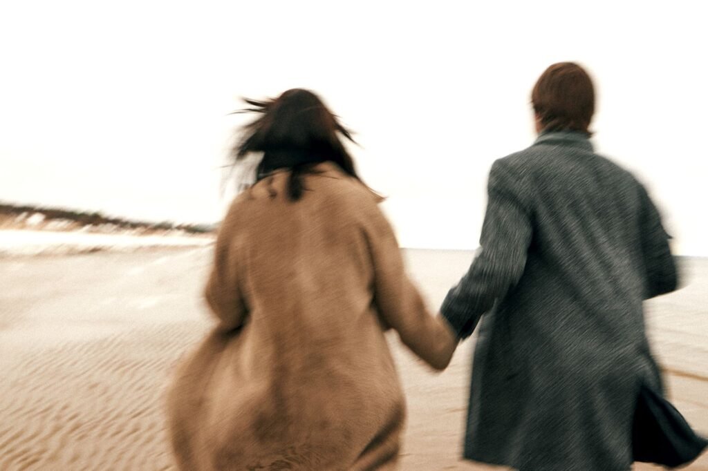 Blurred motion image of a couple holding hands and walking on a sandy beach.