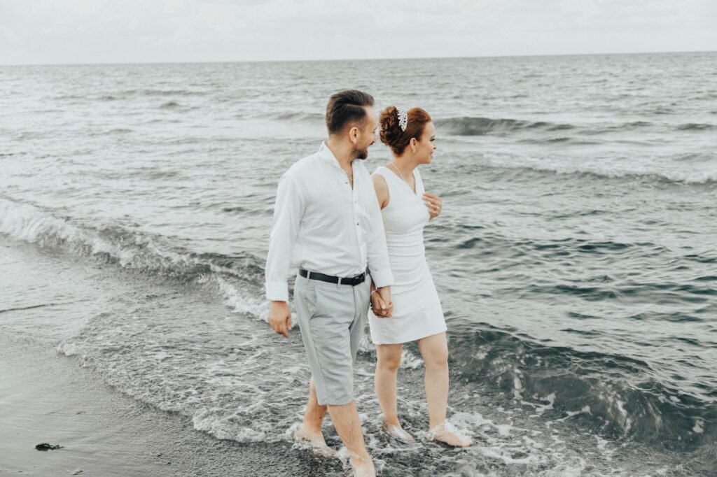 Newlyweds walking barefoot on a beach, enjoying the serene seaside view.