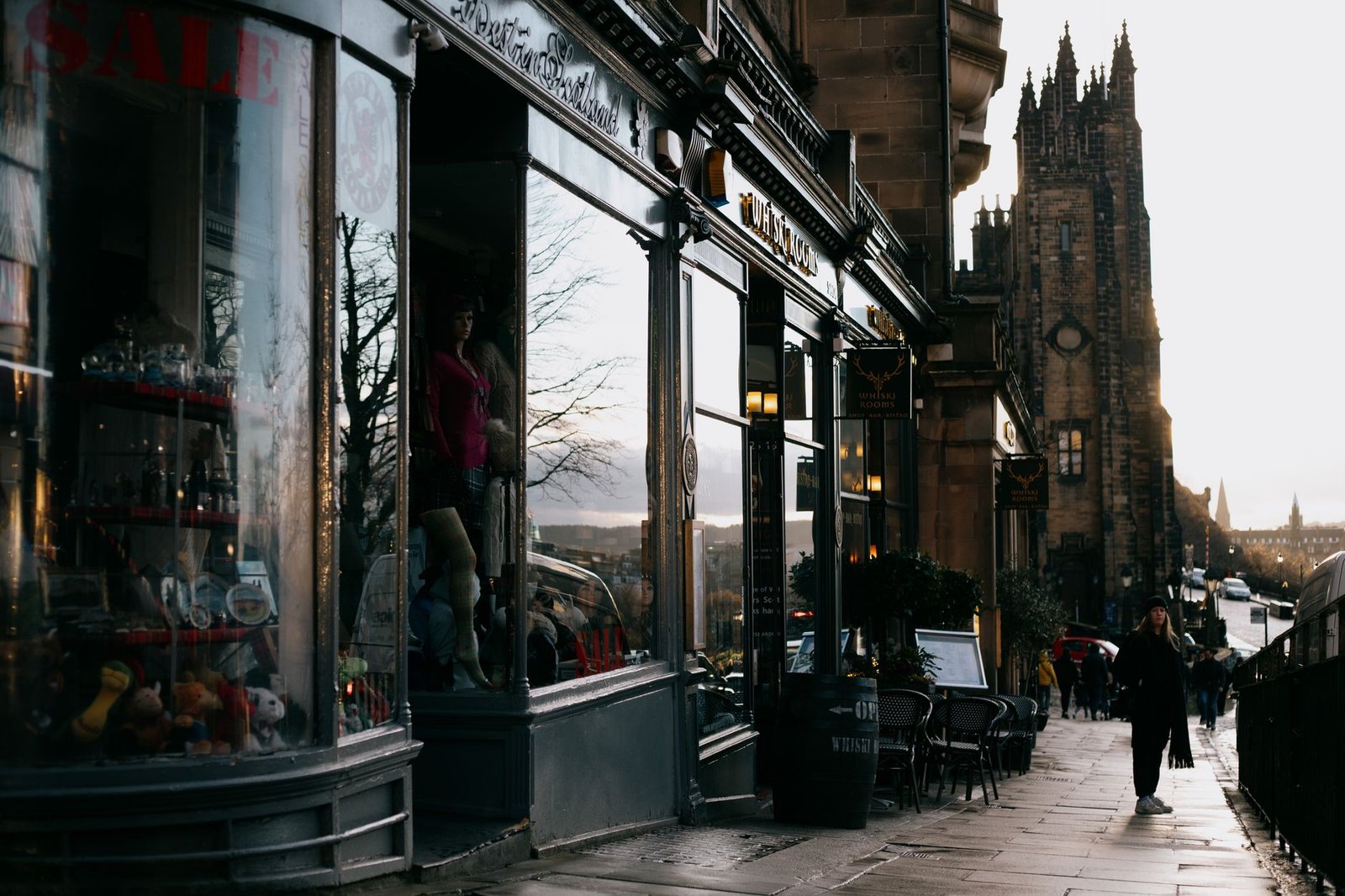 Unrecognizable people on sidewalk near aged building facades and shop with glass walls reflecting leafless tree