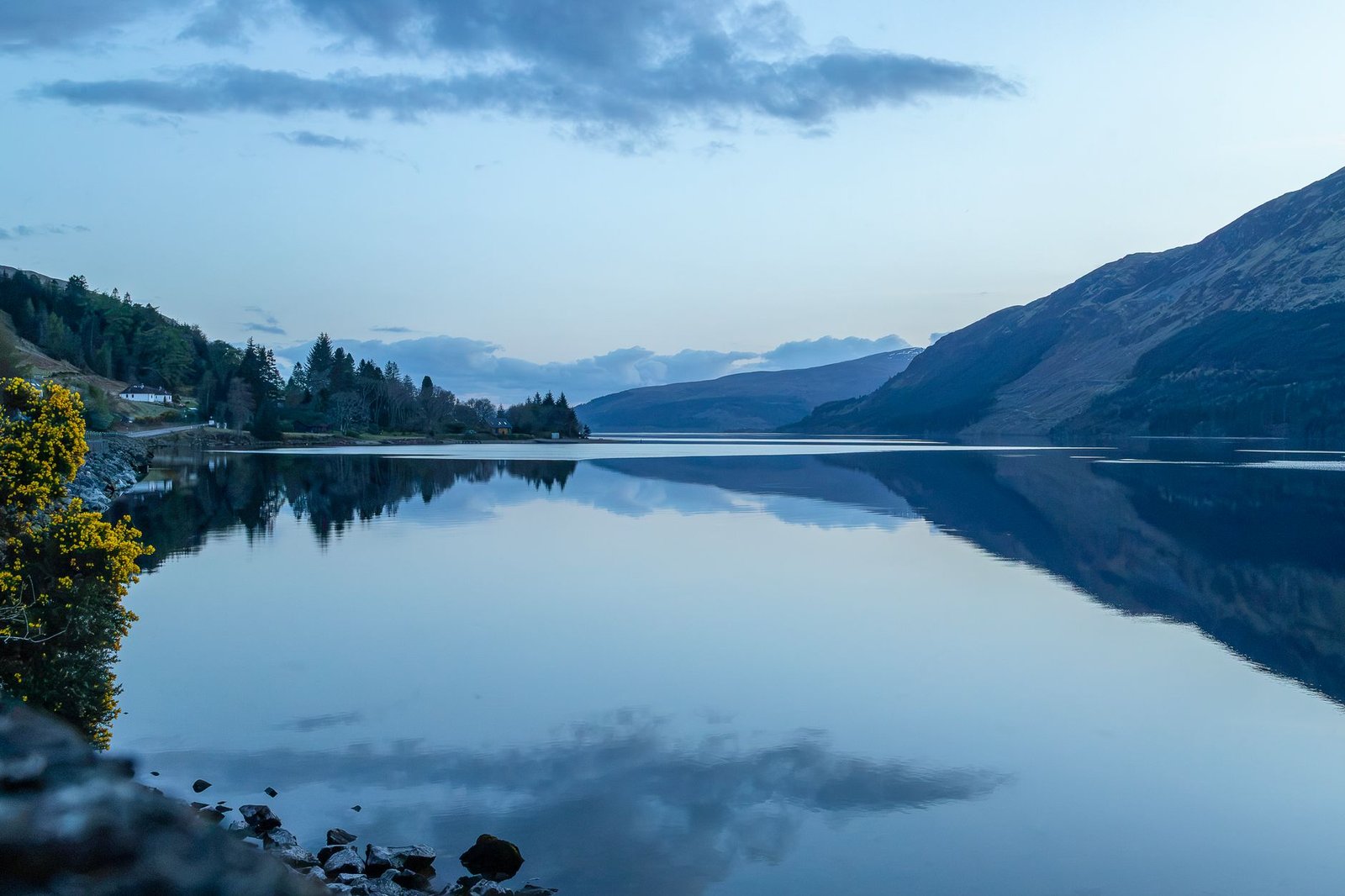 A serene view of a tranquil lake reflecting hills and sky at twilight in the Scottish Highlands.
