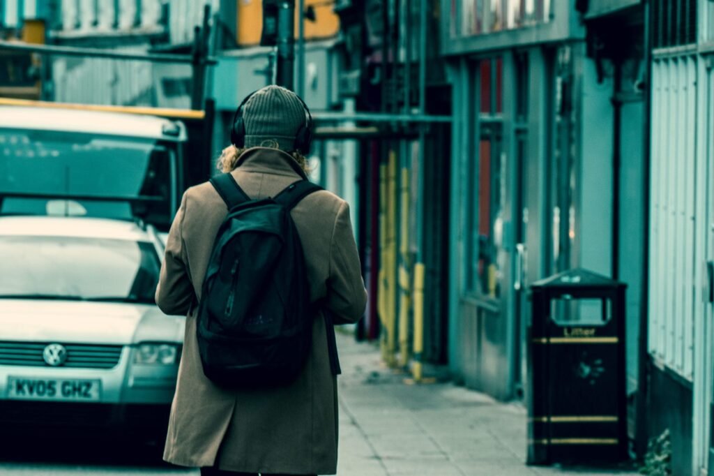 A person in a coat and beanie walks down a city street wearing headphones.