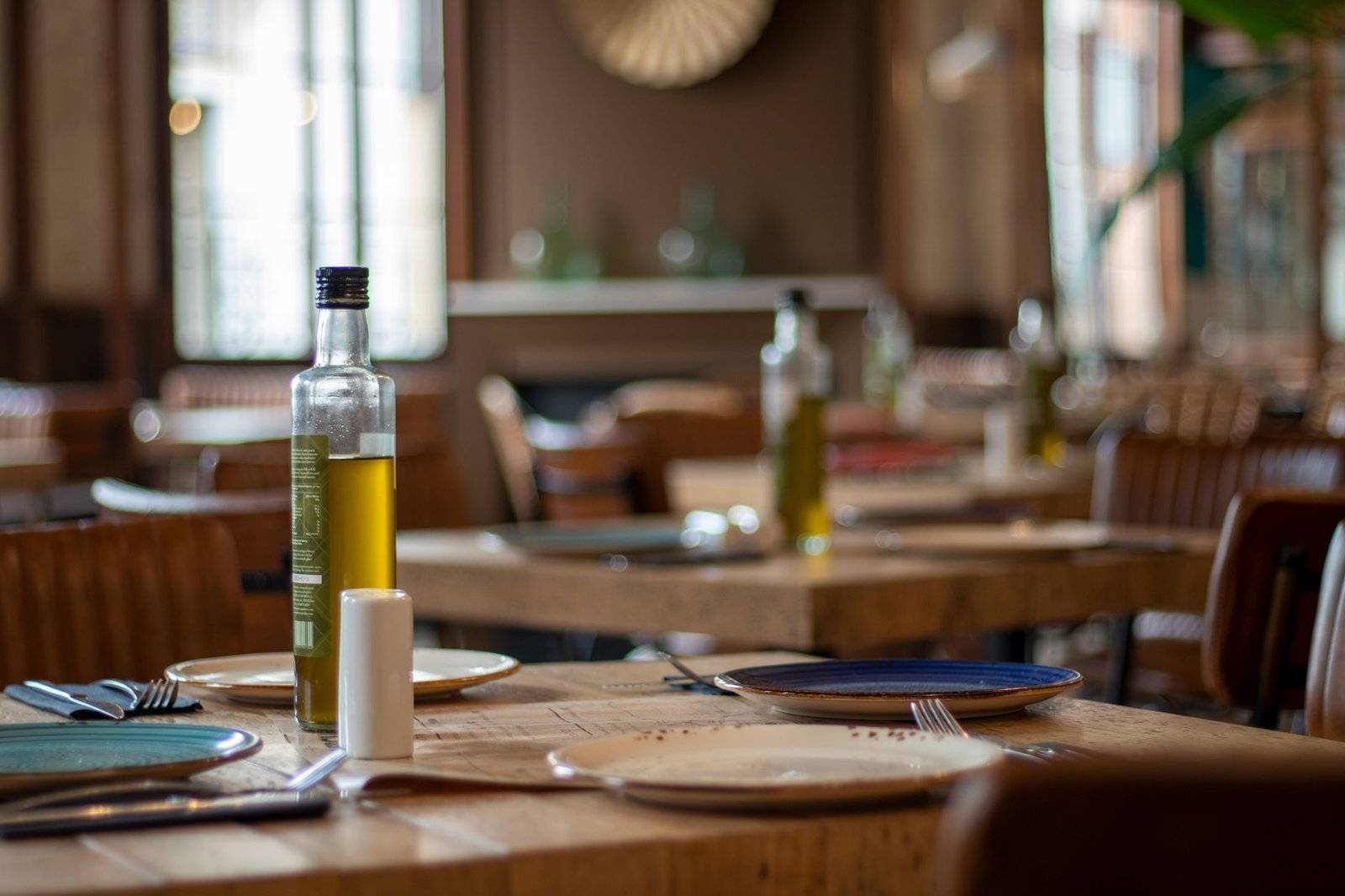 Warm restaurant interior featuring tables set with plates, cutlery, and olive oil.