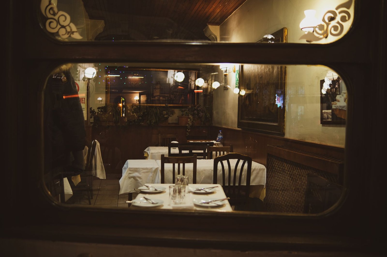 Warm and inviting vintage restaurant interior seen through a window at night with elegant table settings.