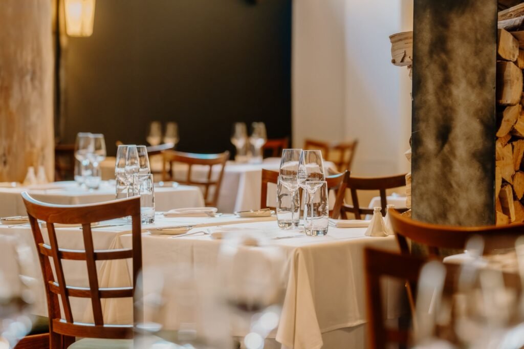 Elegant table setting in a cozy restaurant interior, featuring wooden chairs and white tablecloths.