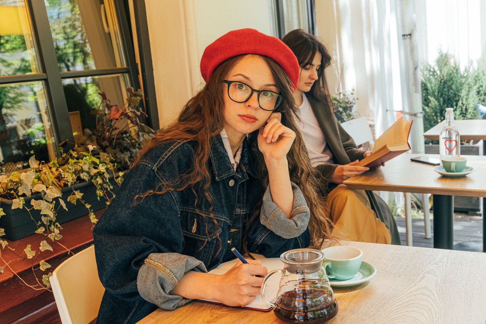 Two women enjoying a cozy café setting, engaged in writing and reading activities.