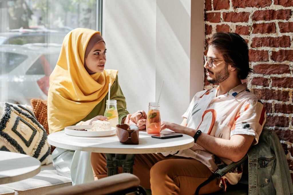 A Muslim couple holding hands at a café, enjoying food and drinks.