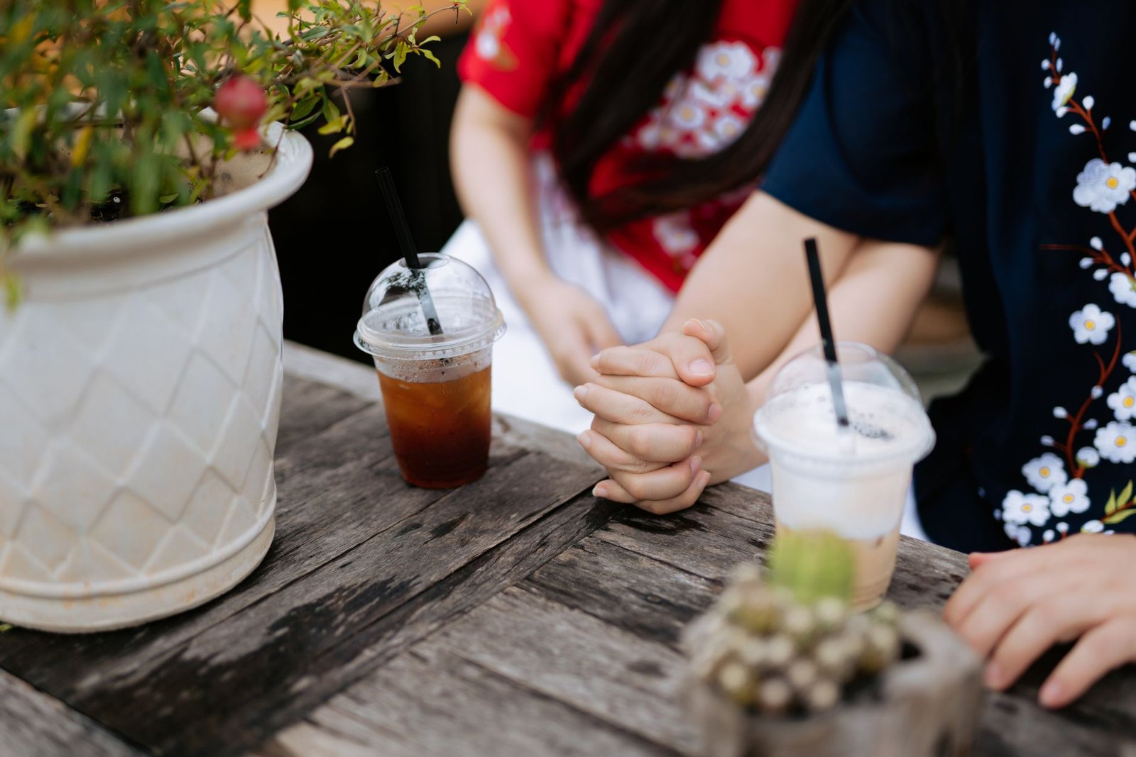 Close-up of a couple holding hands over drinks on a wooden table, capturing a tender moment.