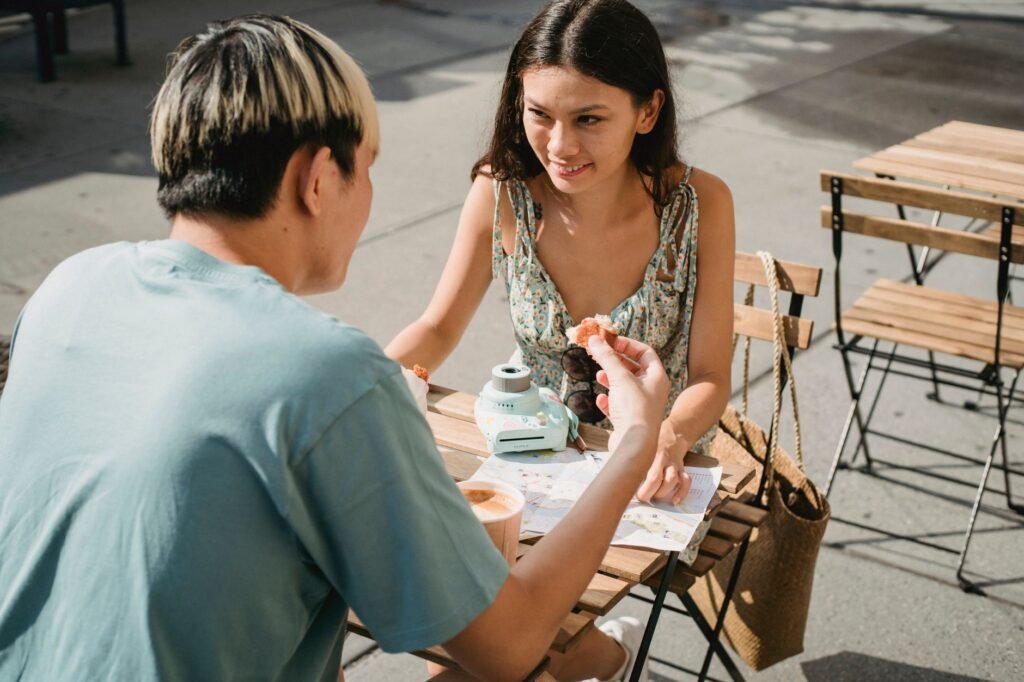 Crop cheerful ethnic female speaking with anonymous partner with pastry and coffee at table in cafe while looking at each oth