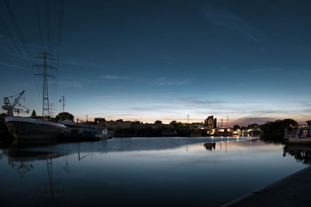 Serene twilight view of a harbor with boats and industrial structures reflecting in calm water.