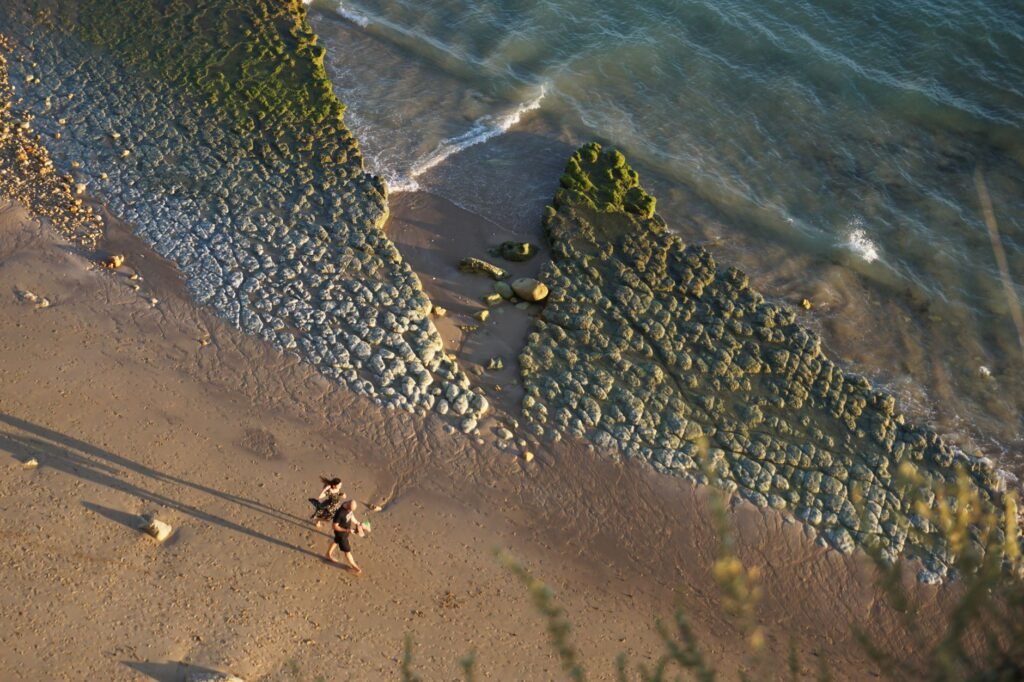 Aerial view of a beach with two people walking along coastal rocks and waves.