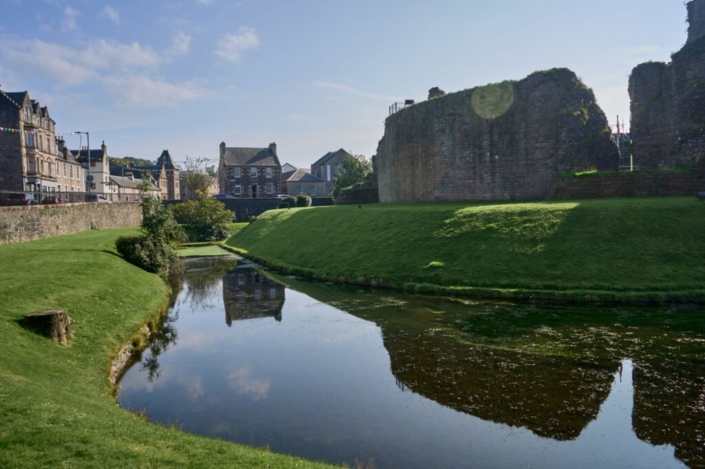 Historic Rothesay Castle with its reflective moat on a sunny day in Scotland, showcasing serene natural beauty.