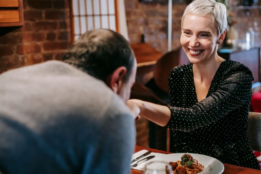 Smiling couple having date while man kissing woman in hand at table with wineglass and plates with pasta with meatballs near