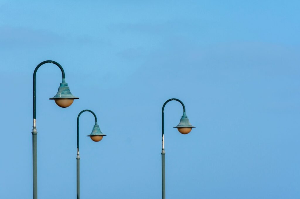 Minimalist image of three retro-style streetlights against a bright blue sky, conveying a summer and open-air feel.