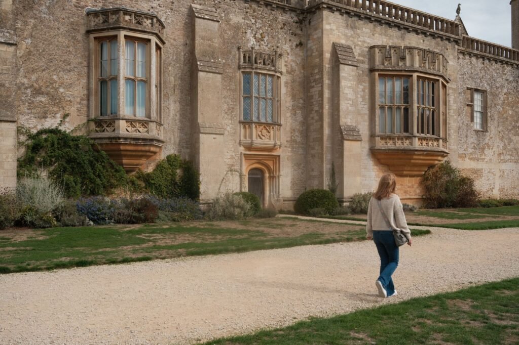 A woman walks by the historic Lacock Abbey, showcasing its stunning architecture.