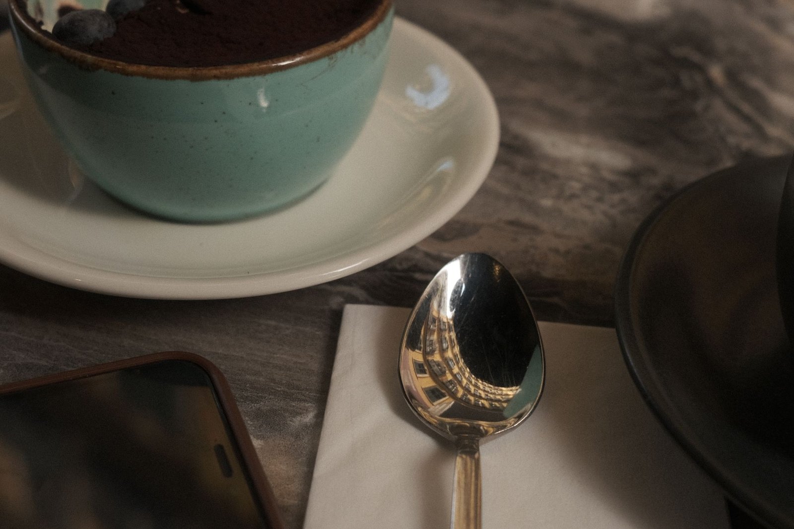 Reflective spoon and dessert on table, capturing café ambiance in İstanbul, Türkiye.