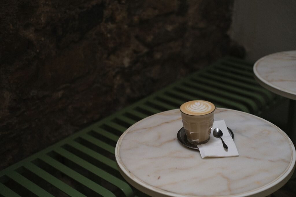 A beautifully crafted latte with delicate latte art sits on a marble table in a cozy café setting. The ambient lighting enhan