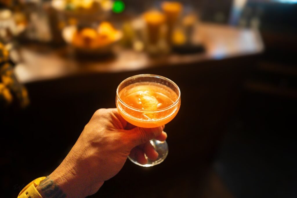 Hand holding a cocktail with orange garnish at a dimly lit Seattle bar. Perfect for lifestyle themes.