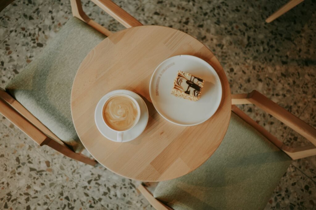 Top view of a coffee cup and dessert slice on a café table with chairs.