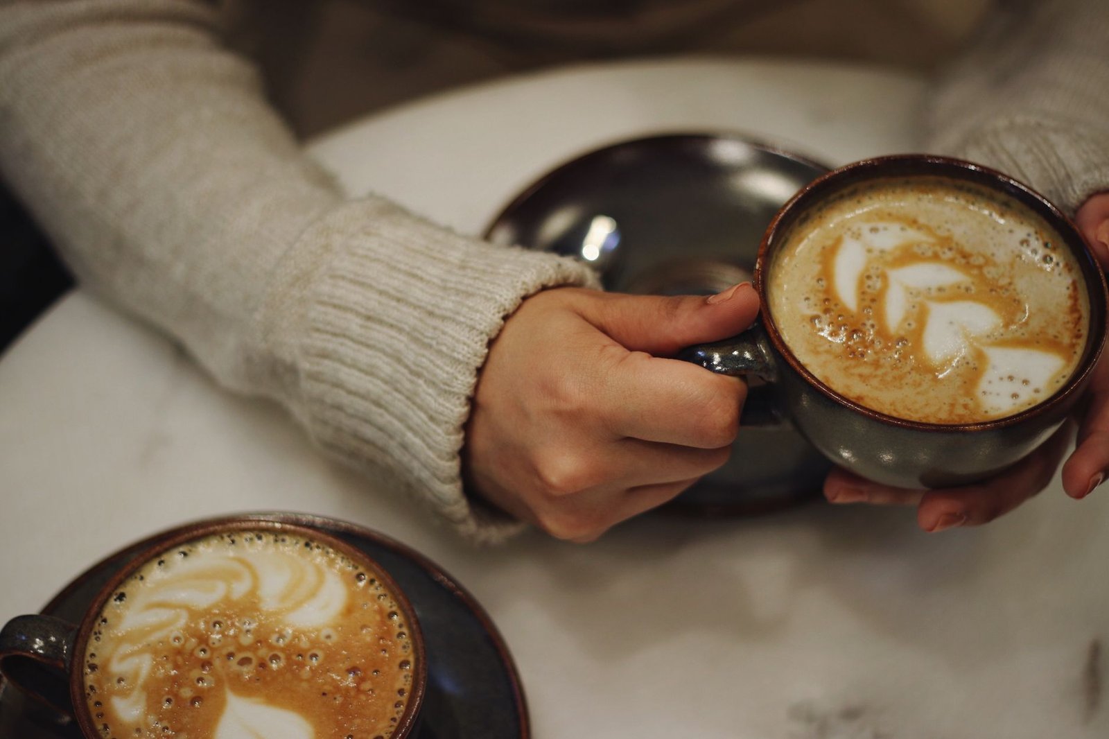 Close-up of hands holding a coffee cup with latte art in a cozy café setting.