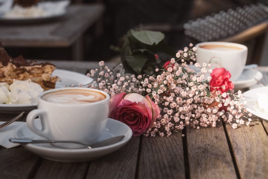 Charming outdoor coffee setting with cappuccino, cake, and roses on a rustic wooden table.