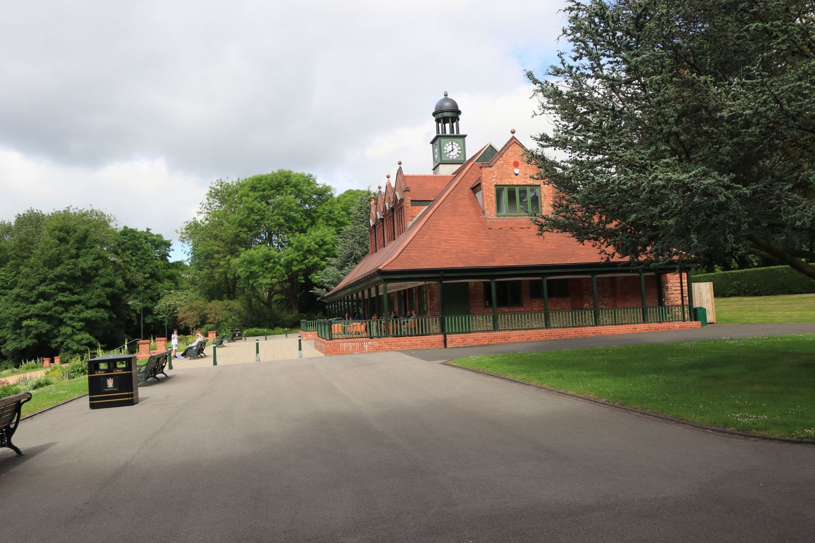 Red brick pavilion with clock, lush greenery in a peaceful park scene, ideal for leisure and outdoor activities.
