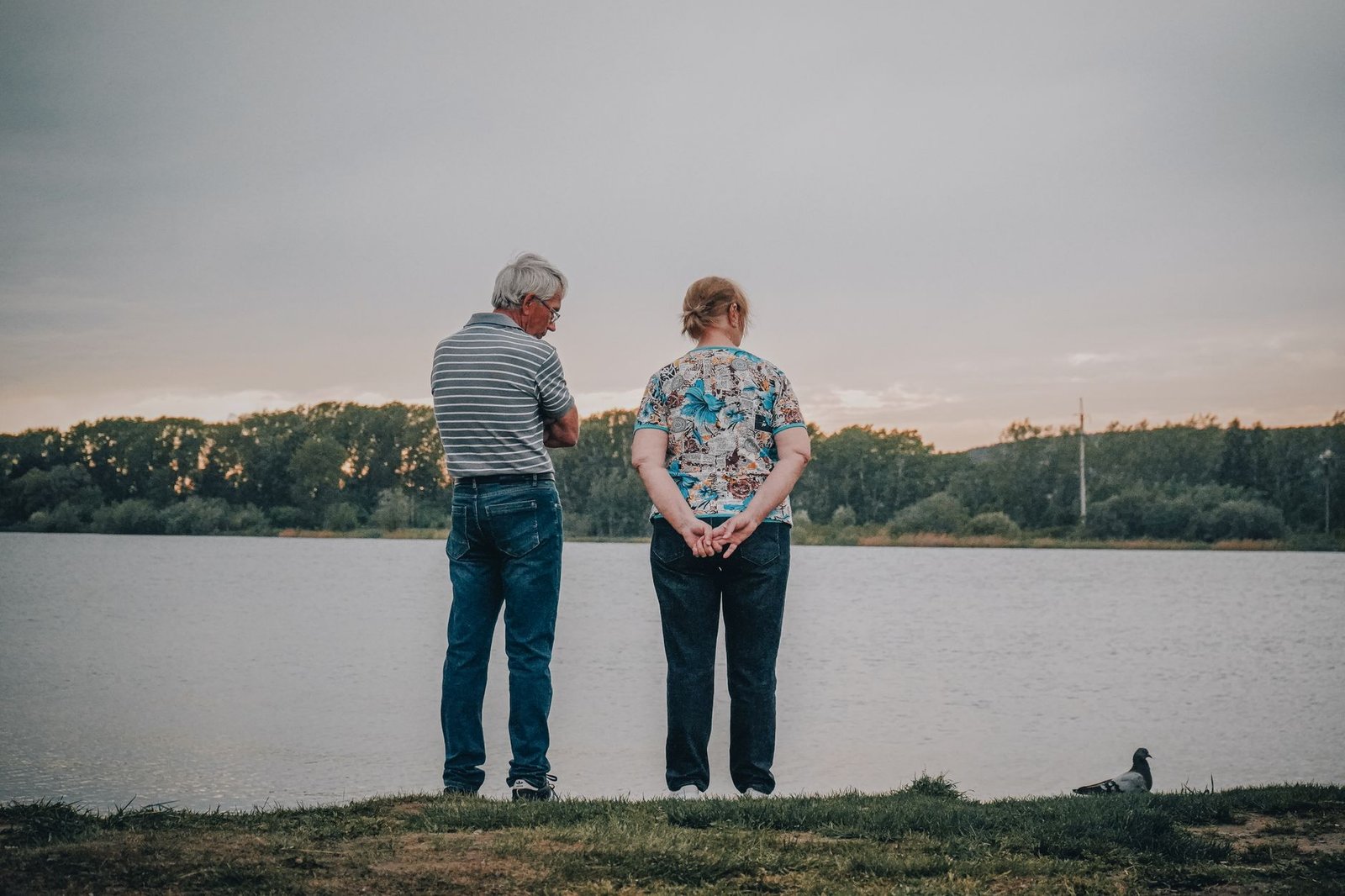 Senior couple standing by a serene lake, enjoying the tranquil outdoor setting together.