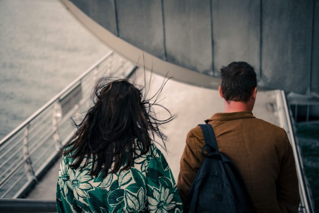 A couple with backpacks walks on a windy city overpass.