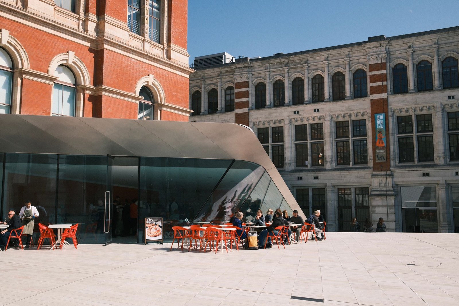 Modern architecture with outdoor seating at a cafe on a sunny day with visitors.