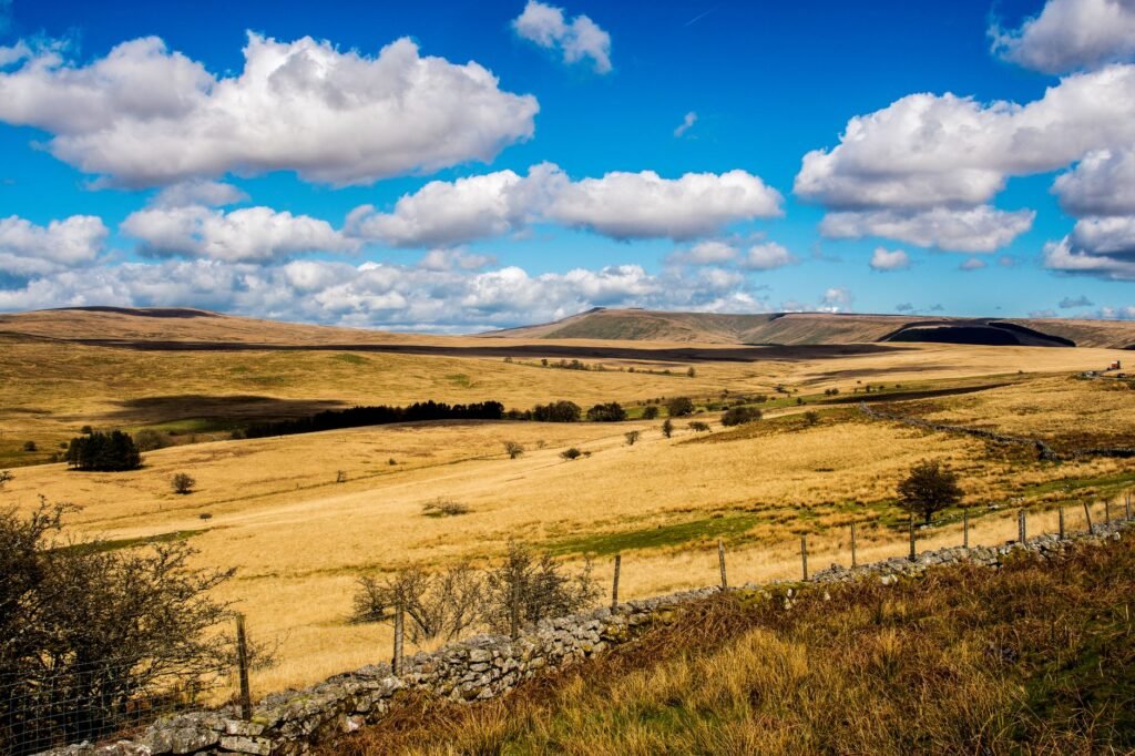 Stunning view of a grassy countryside landscape with hills under a blue cloudy sky.