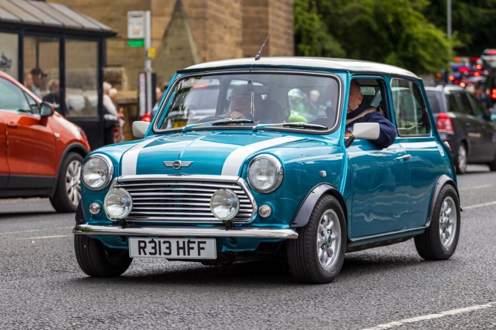 A vintage blue Mini car driving on a street in Morpeth, England, showcasing classic British automotive design.