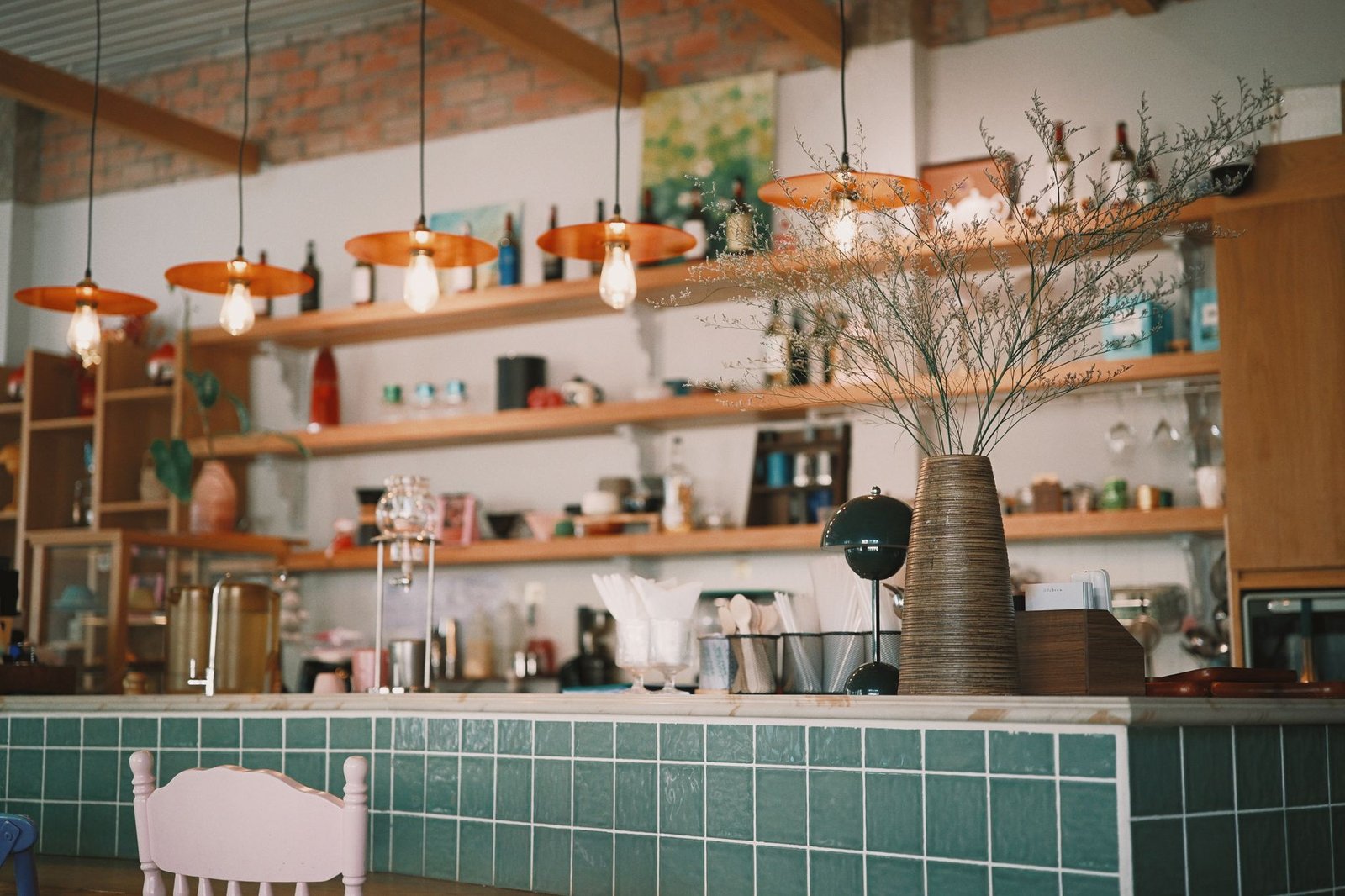 A stylish coffee shop interior featuring pendant lights and decorative vases on green tiled counter.