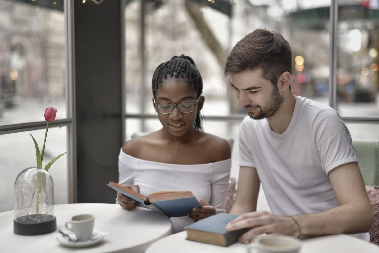 A couple enjoys reading books together in a cozy café setting with coffee and flowers around.