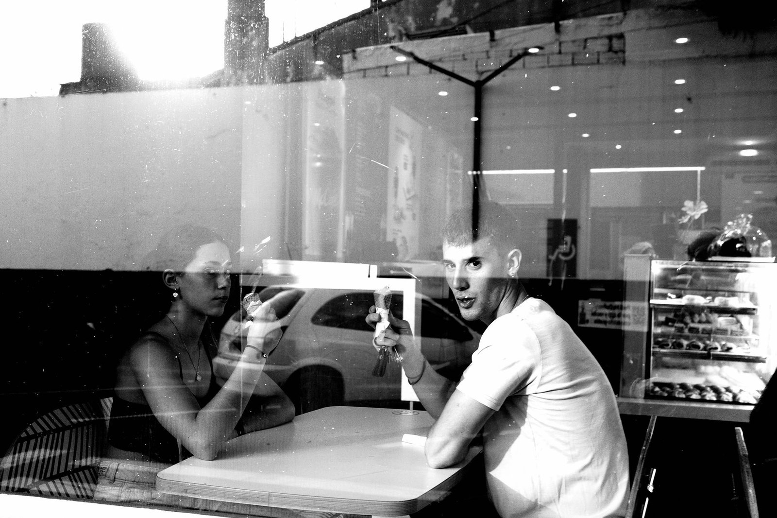 A black and white reflection of two people talking in a café through a window.