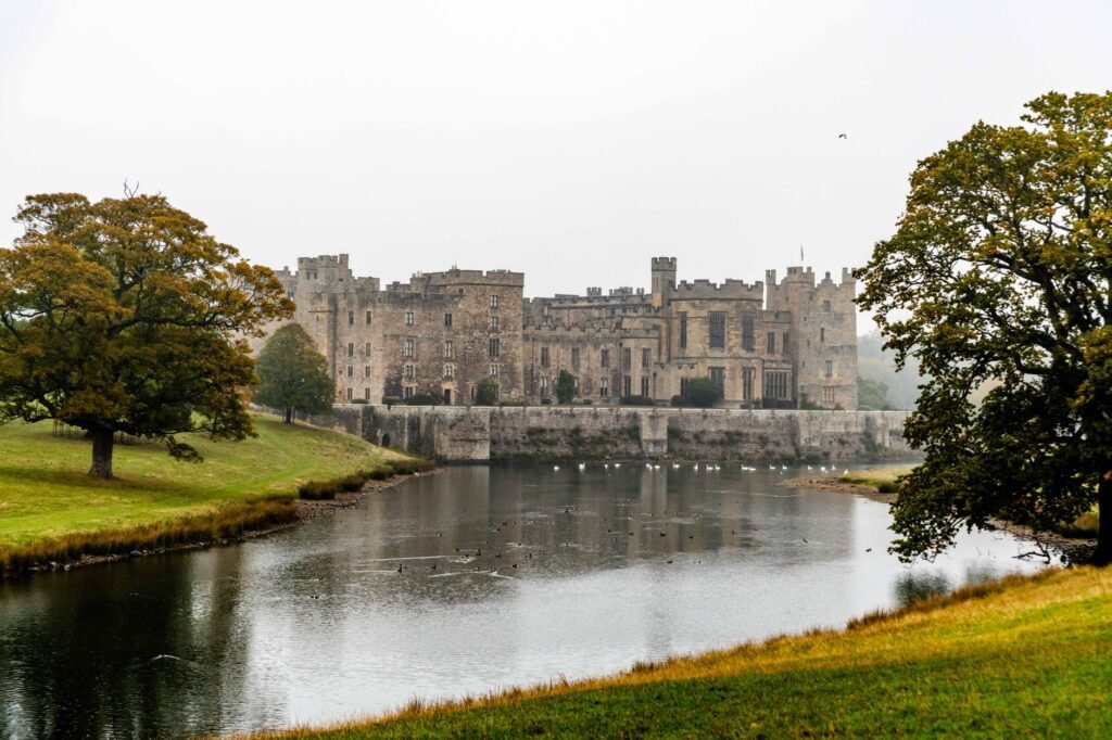 View of Raby Castle reflecting in a tranquil lake surrounded by lush green landscape.