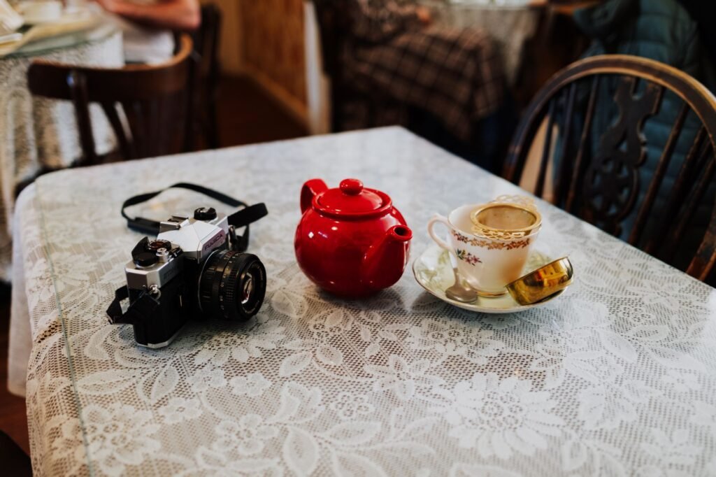 Red teapot, vintage camera, and teacup on floral lace tablecloth in cozy cafe.