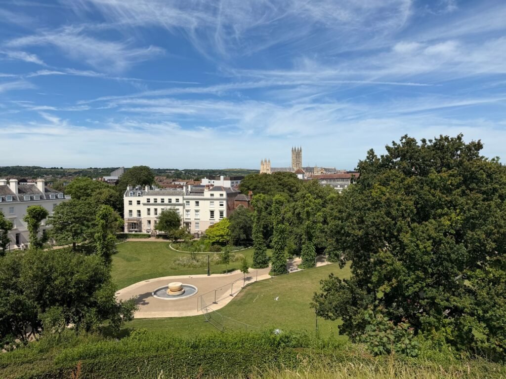 A picturesque view of Canterbury Cathedral with surrounding gardens and historic buildings under a vibrant sky.