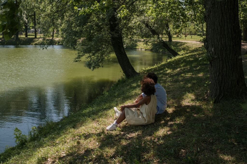 A young couple enjoying a serene moment by a pond in a lush, sunny park setting.