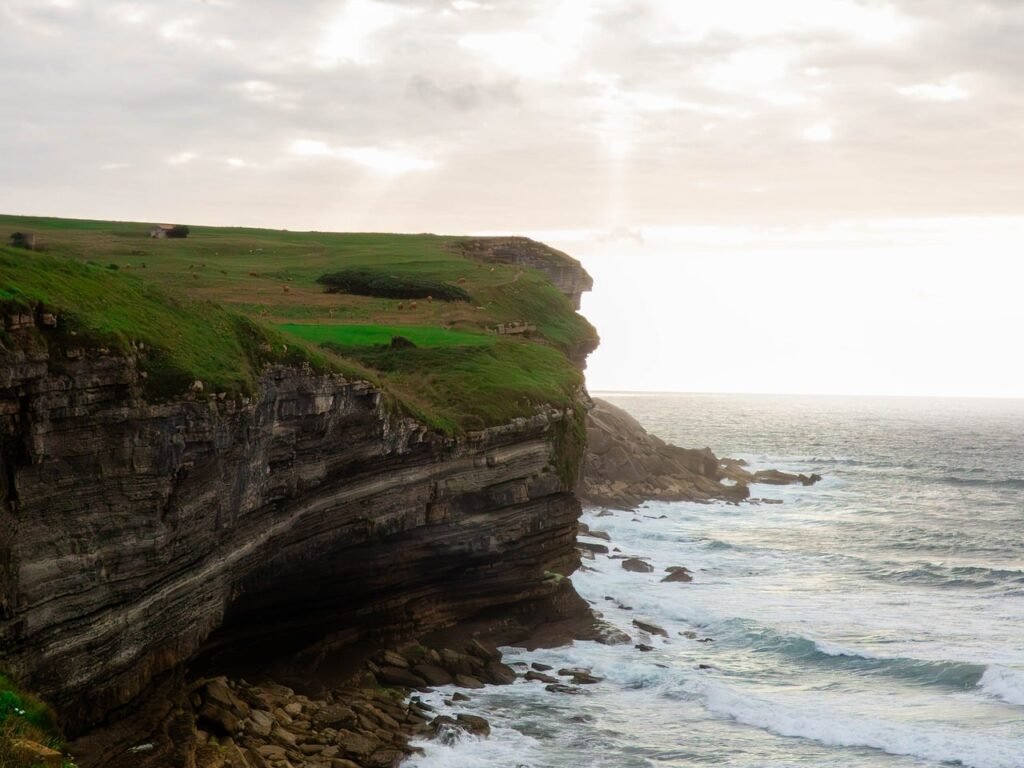 sea cliffs, ocean waves, coastal landscape, green fields, cloudy sky, dramatic landscape, rocky coast, natural scenery, ocean