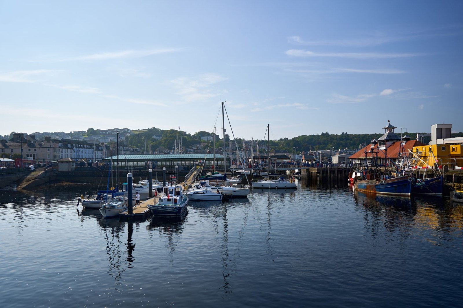 Idyllic harbor scene in Rothesay, Scotland with boats docked under a clear summer sky.