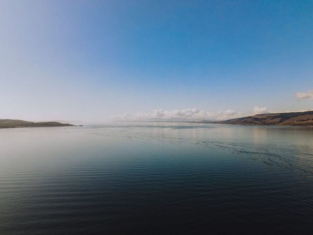 Serene landscape of water and hills under a blue sky in Greenock, Scotland.