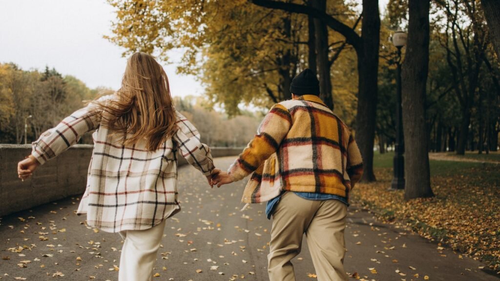 Couple enjoying autumn day running through a park holding hands.