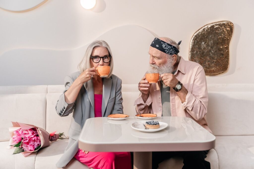 Elderly couple sitting in a cafe enjoying coffee with a flower bouquet beside them.
